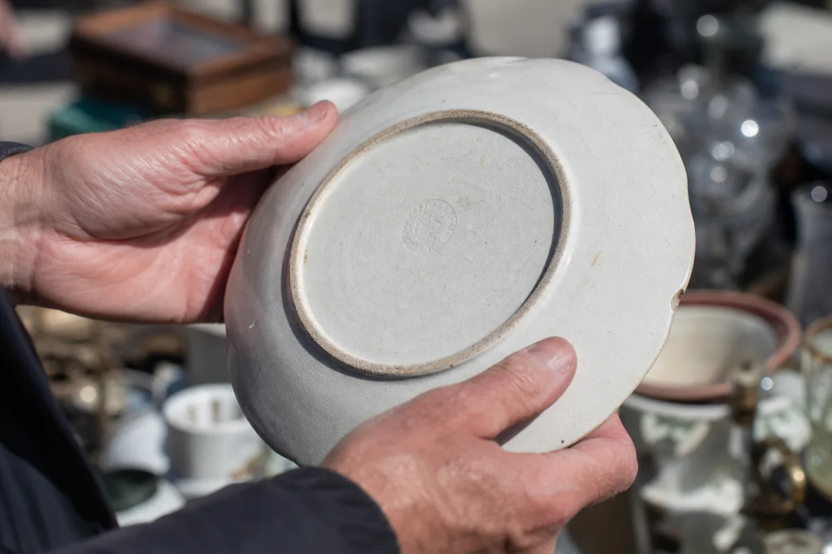 Acheteur inspectant un objet sur un étal de vide-grenier ensoleillé
