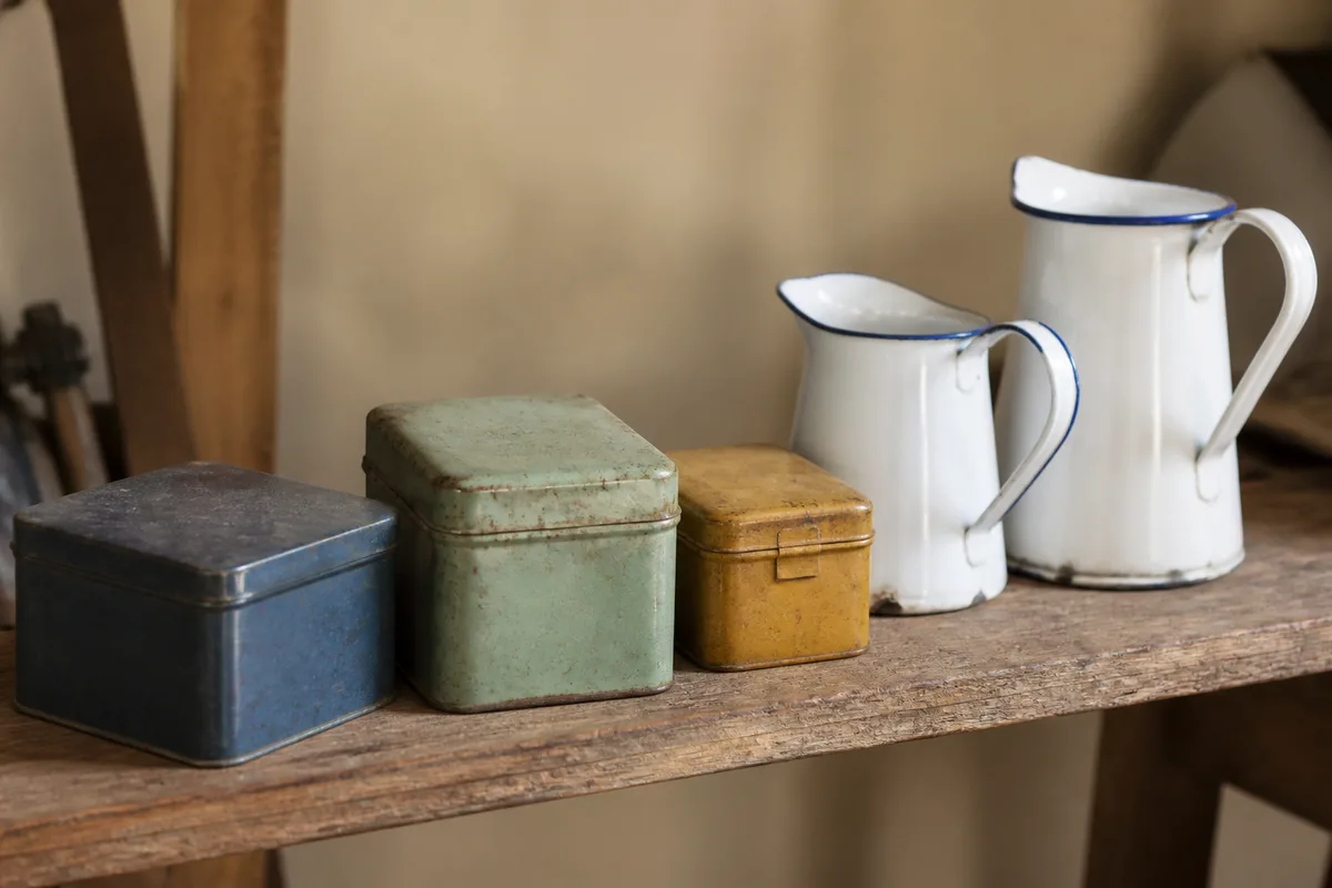 Boîtes métalliques patinées et brocs émaillés alignés sur une étagère en bois brut