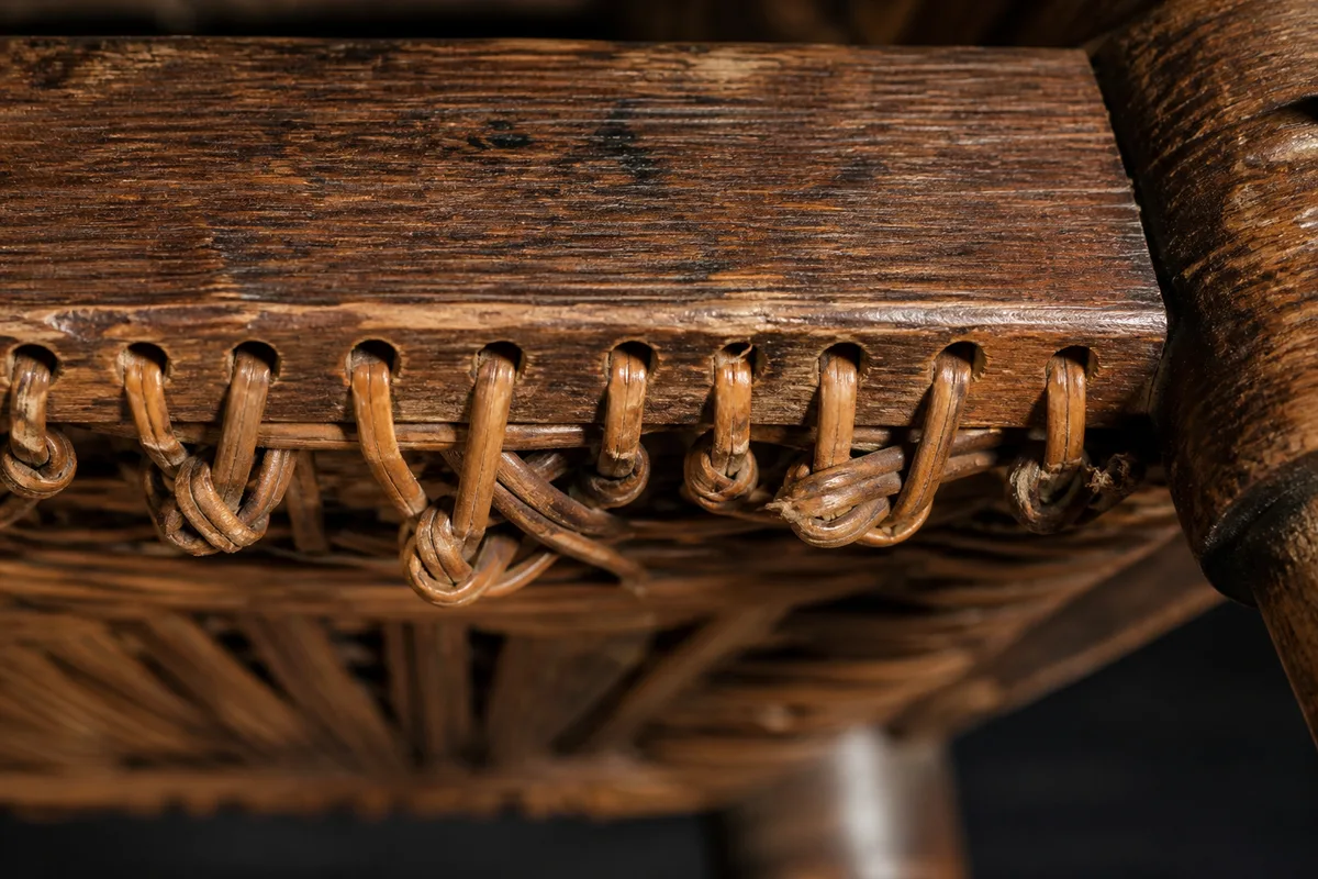 Dessous d’une chaise ancienne montrant les trous percés du cadre et les brins de rotin